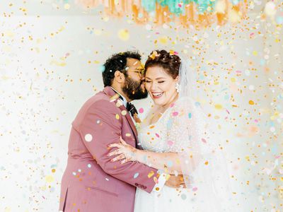 Groom kissing brideâs cheek surrounded by colorful confetti