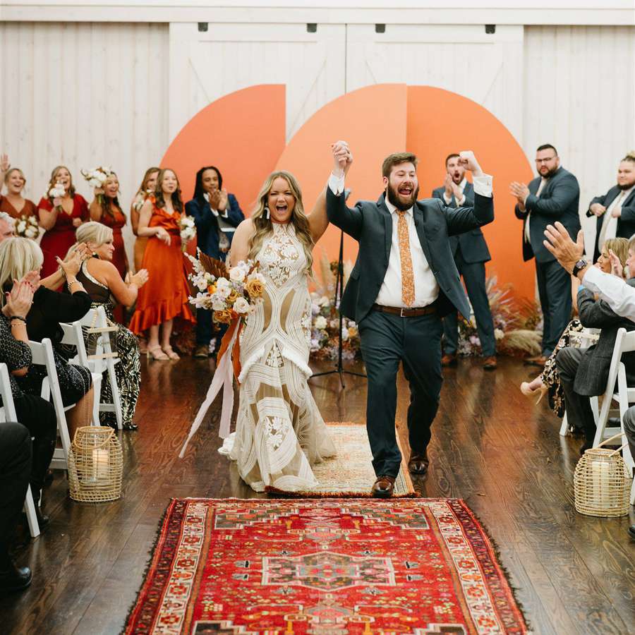 Bride and groom celebrating during their recessional, accompanied by geometric rug and colorful arch backdrop