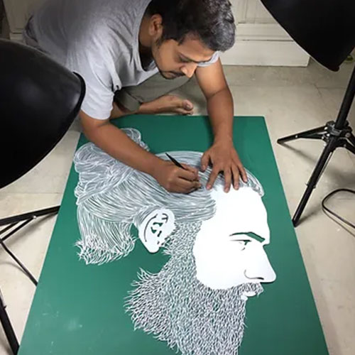 Parth Kothekar works on a paper cut portrait while sitting cross legged on the floor 