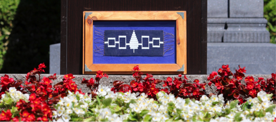 A framed Hiawatha Wampum Belt flag sits in front of a garden at McGill. 
