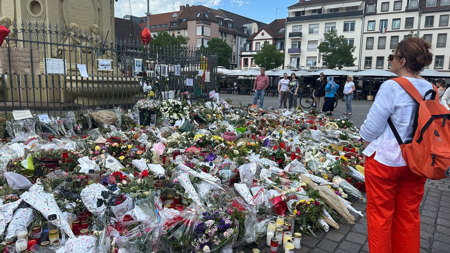 Blumen und Blumensträuße vor Brunnen auf Marktplatz Mannheim, Frau steht daneben und trauert