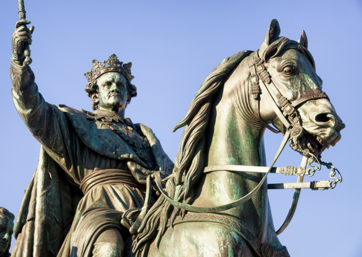 La estatua de un rey lo muestra sujetando un cetro en alto mientras está sentado sobre su caballo.