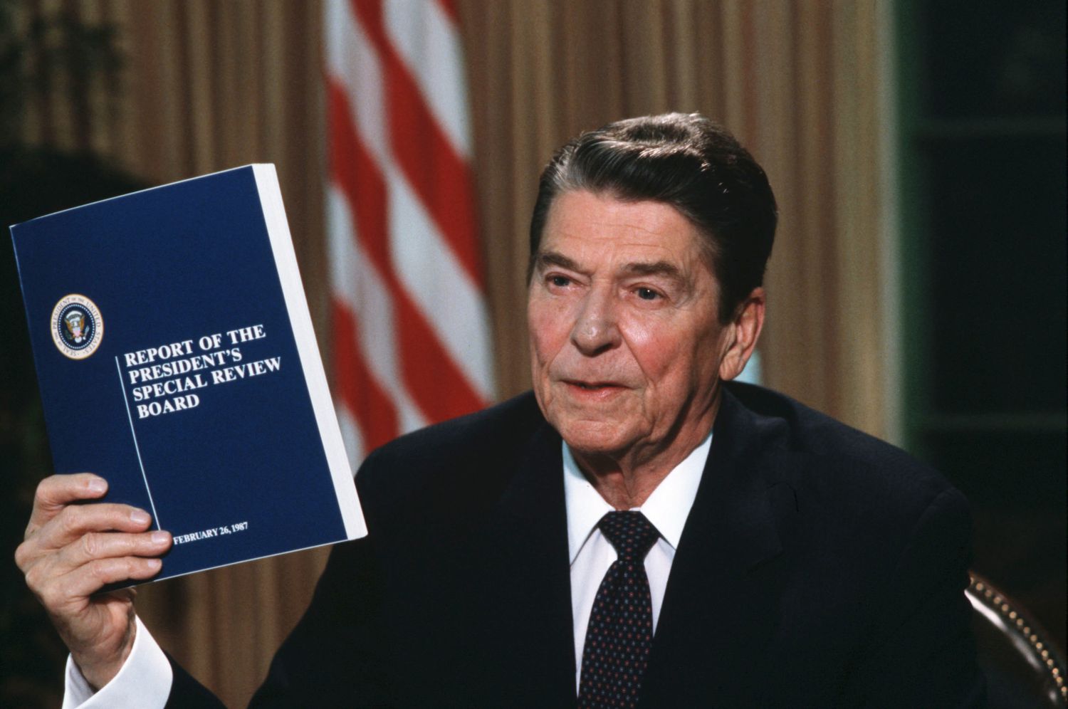 President Ronald Reagan holding a copy of the Tower Commission report on the Iran-Contra scandal