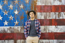 A young hipster man stands before an American flag. Find out what makes Americans stand out from others.