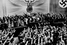 Hitler receives an ovation after announcing the Anschluss, black and white photograph with people saluting.