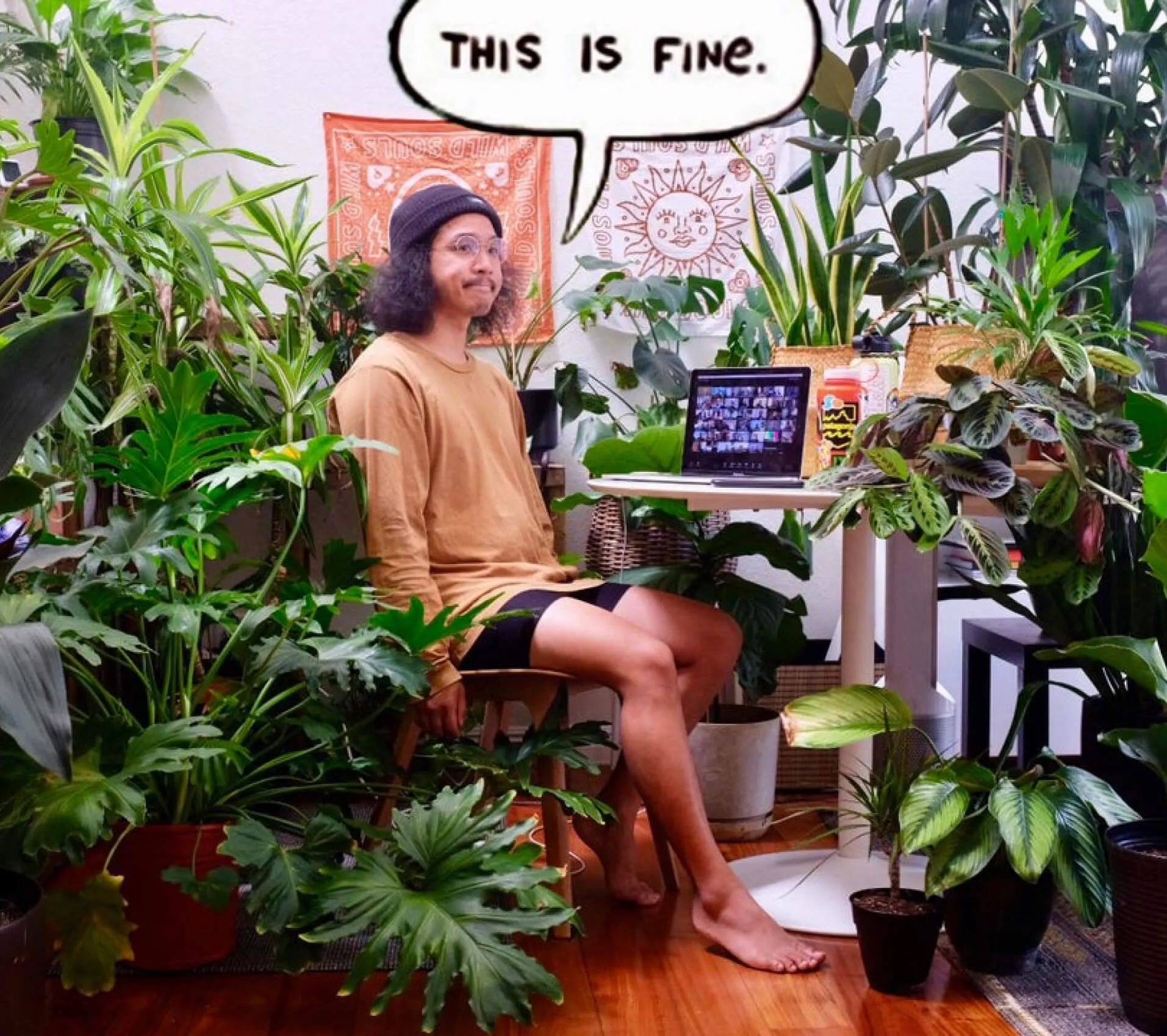 A person sitting at a desk in a room full of plants with a speech bubble that reads "This is fine."