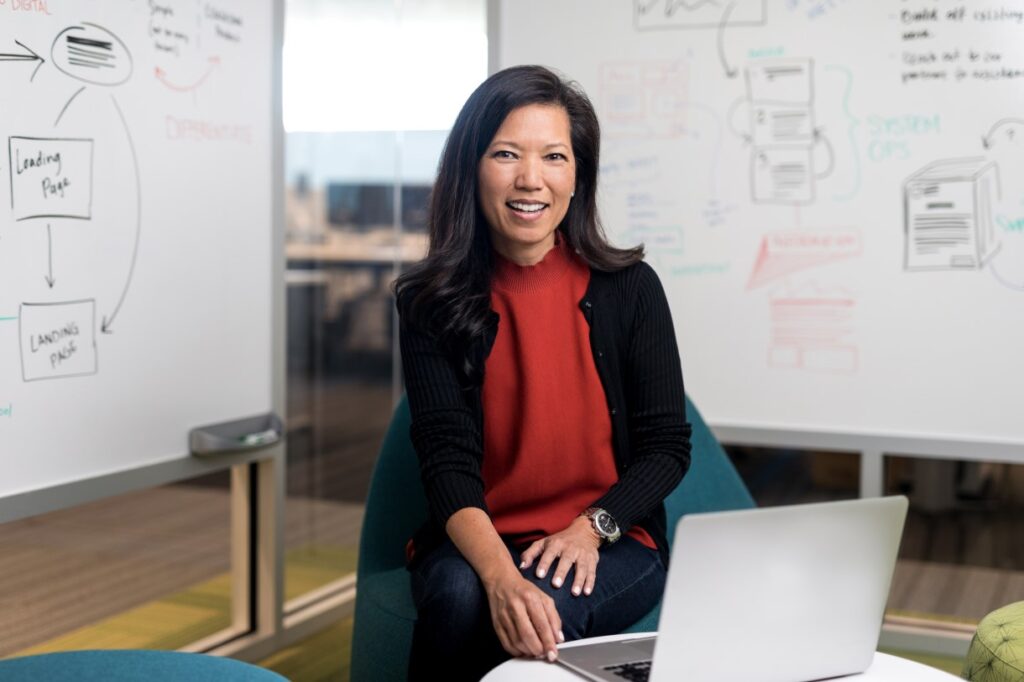 a woman sitting at a desk with a laptop and smiling at the camera