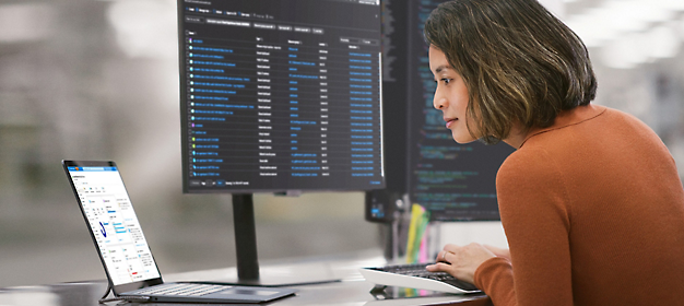 Woman analyzing data on computer screens in an office setting.