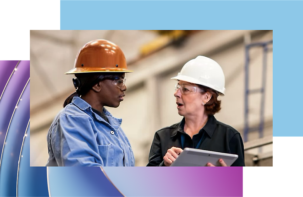 Two professionals wearing hard hats discussing work in an industrial setting.