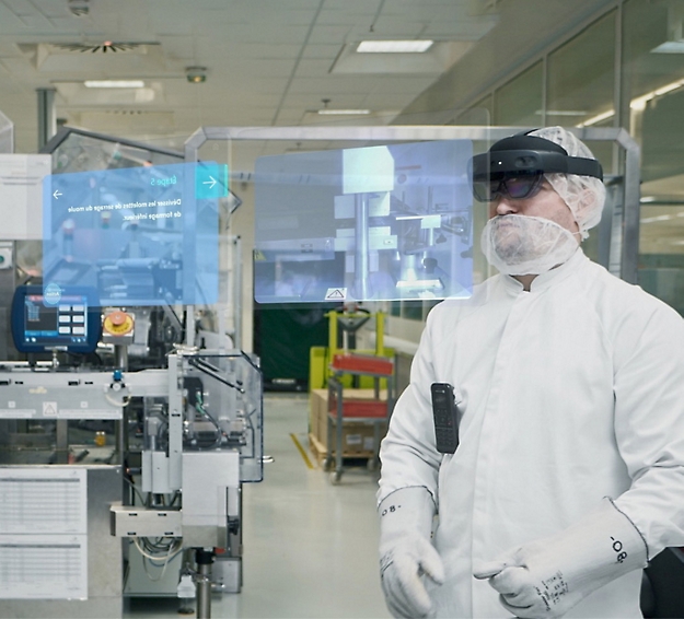 A man wearing a lab coat, hairnet, and augmented reality glasses stands in an industrial setting with virtual interfaces.