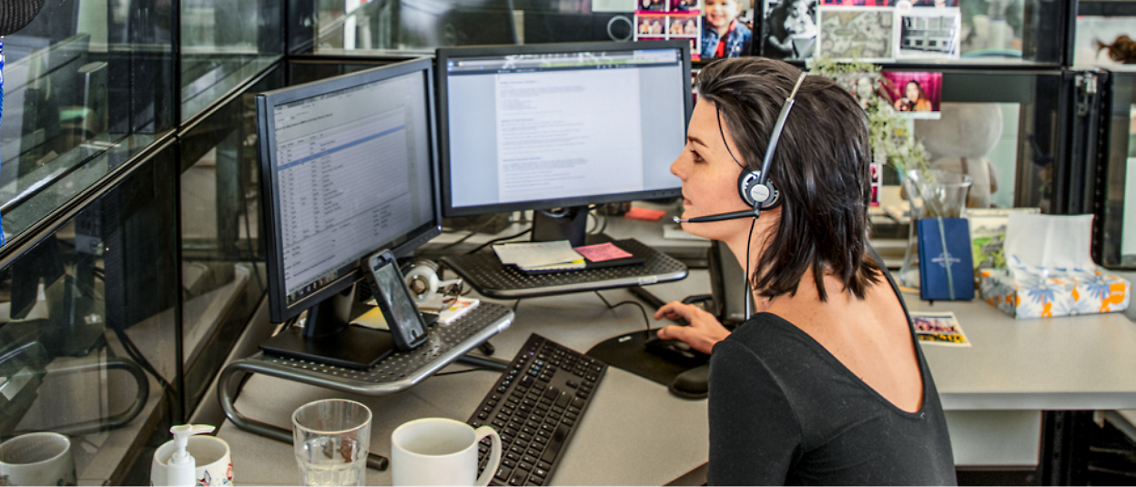 Eine Person, die ein Headset trägt und an einem Schreibtisch mit mehreren Computerbildschirmen sitzt