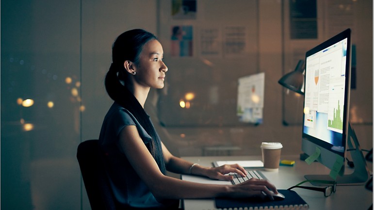 A person working on a desktop in a glass office at night.