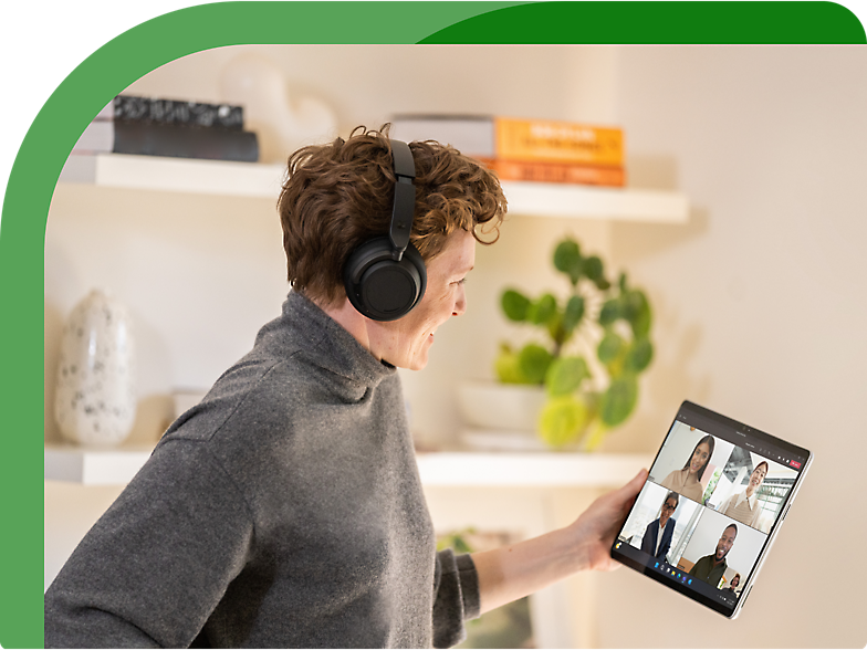 A woman wearing headphones is holding a tablet with a video call on it.
