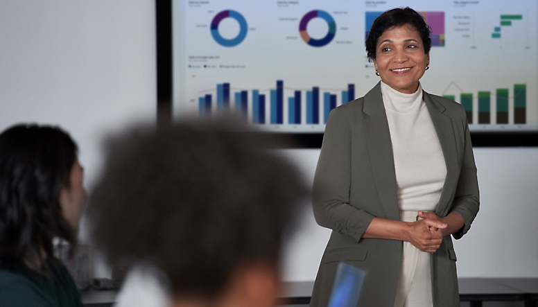 A woman in a business suit standing in front of a screen with graphs on it.