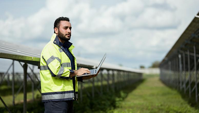 A man with a laptop in front of solar panels.