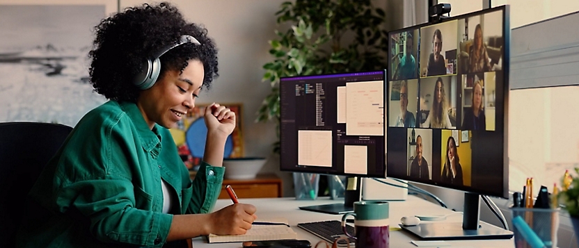 A woman on video call with headphones and also writing something in a notebook