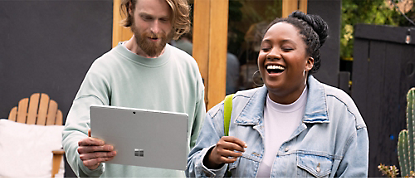 A man and woman laughing while holding a microsoft surface tablet.