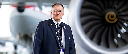 Ein Mann im Anzug steht vor einem Flugzeugtriebwerk.