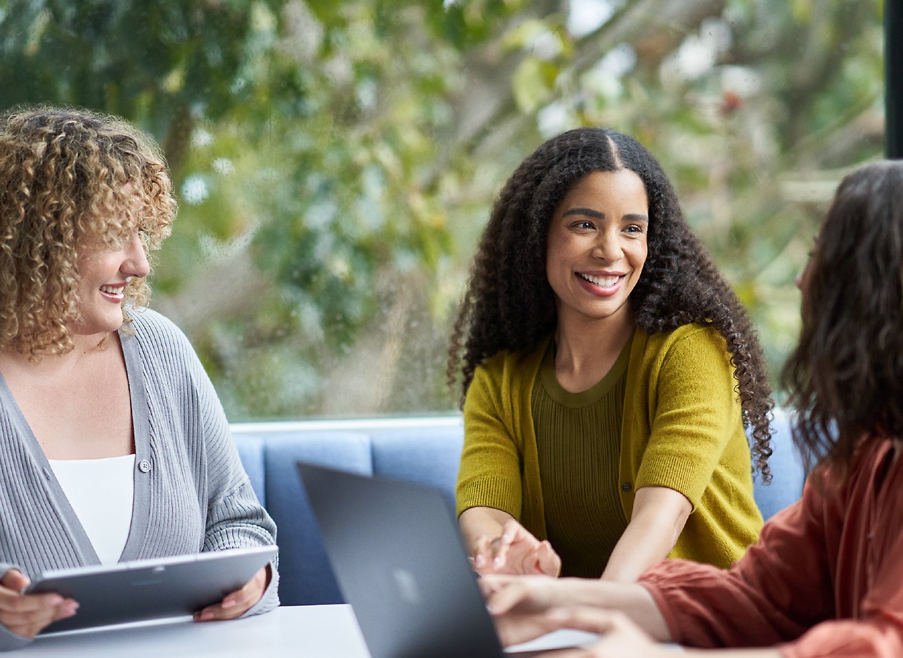 Three persons looking and smiling at each other with laptop in front of them.