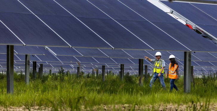 Two people walk next to solar panels, one of them points ahead.