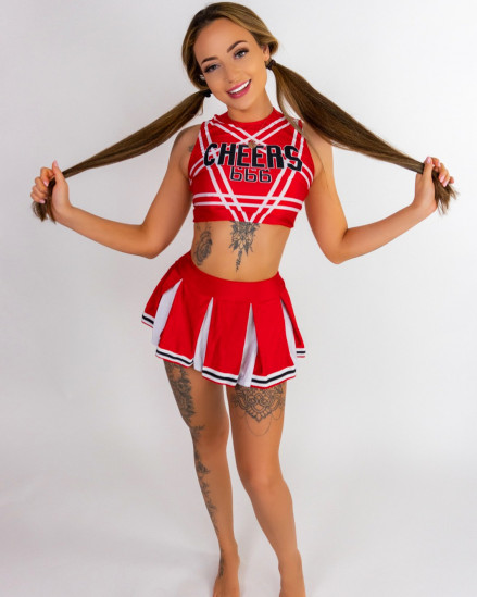 Poppy May Babestation holds out her pigtails dressed as a cheerleader barefoot