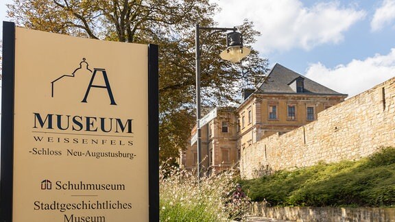 Ein Schild weist auf das Museum in Schloss Neu-Augustusburg in Weißenfels hin, am rechten Bildrand sind Teile des Schlosses zu sehen.