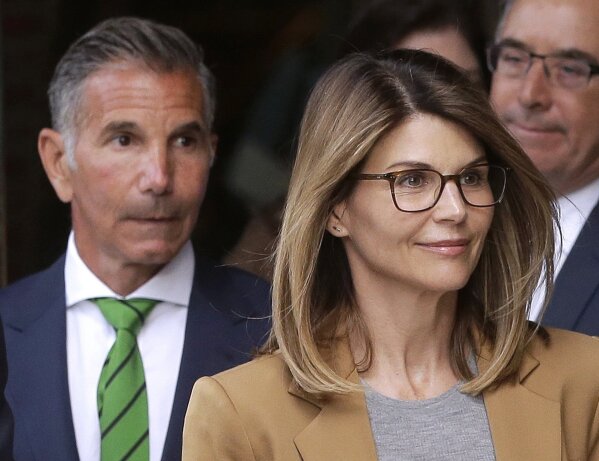 CORRECTS THAT GIANNULLI IS UNDER HOME CONFINEMENT - FILE - In this April 3, 2019, file photo, actress Lori Loughlin, front, and her husband, clothing designer Mossimo Giannulli, left, depart federal court in Boston after facing charges in a nationwide college admissions bribery scandal.    Giannulli has been released from a California prison, Saturday, April 3, 2021,  and is under home confinement following his imprisonment for his role in a college admissions bribery scheme.  (AP Photo/Steven Senne, File)