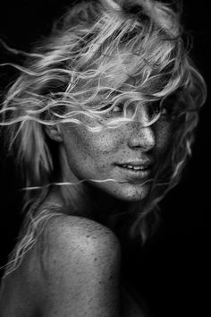 a black and white photo of a woman with frizz on her face, hair blowing in the wind