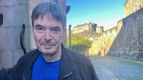 Sir Ian Rankin stands in a lane in Edinburgh 