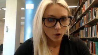 Nettes blondes College-Mädchen, das in der Bibliothek blinkt