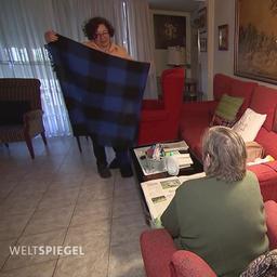 Eine Frau legt in einem Wohnzimmer eines älteren Mannes eine Decke zusammen