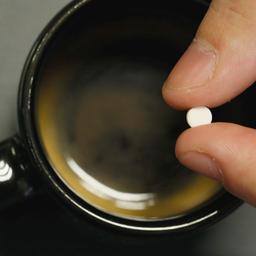 Eine Tablette mit Aspartam Zuckerersatz wird über eine Tasse mit Kaffee gehalten.