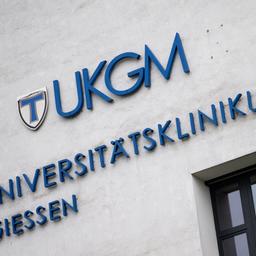 Blauer Schriftzug "UKGM Universitätsklinikum Gießen" an einer grauen Hauswand.