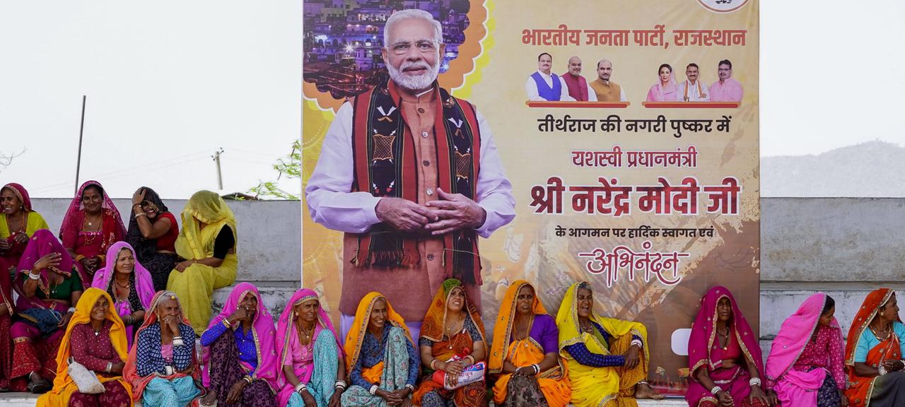 Frauen sitzen vor einem Wahlplakat von Narendra Modi.