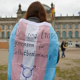 Eine Aktivistin steht vor dem Reichtstagsgebäude mit einer Pride-Flagge mit der Aufschrift "Cis und trans - gemeinsam für Selbstbestimmung".