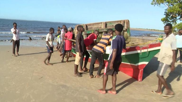 Menschen stehen um ein Fischerboot am Strand von Mosambik 