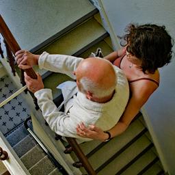 Eine Frau unterstützt einen älteren Mann beim Treppensteigen in einem Treppenhaus.