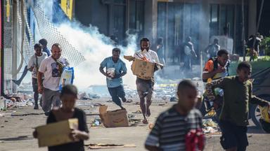 Menschen rennen in Port Moresby mit geplünderten Waren umher.