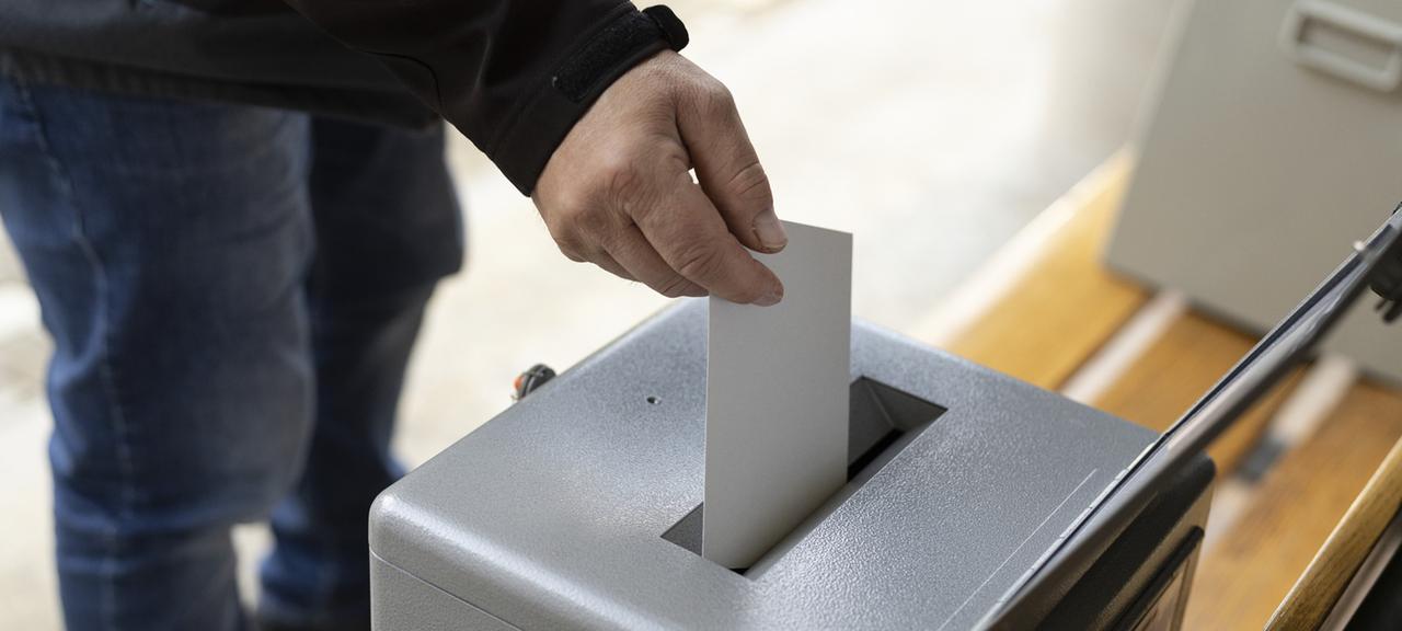 Ein Mann wirft einen Stimmzettel in eine Urne (Nahaufnahme)