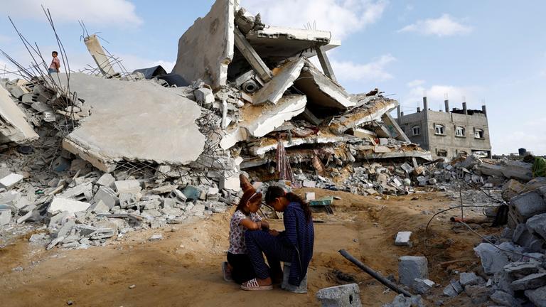 Zwei Kinder sitzen neben einem zerbombten Haus.
