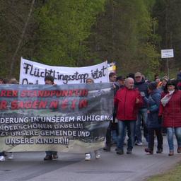 Rund 170 Menschen haben sich zu einem Protestmarsch in der Gemeinde Dabel versammelt. Sie demonstrieren gegen eine geplante Geflüchtetenunterkunft und gehen Banner schwingend über einen asphaltierten Weg im Dorf.