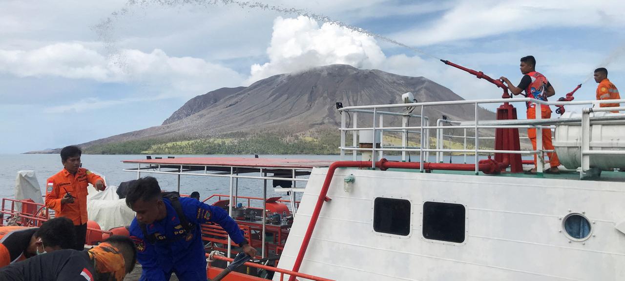 Ein Schiff mit Einsatzkräften liegt am Pier. Im Hintergrund ist der Vulkan Ruang zu sehen.