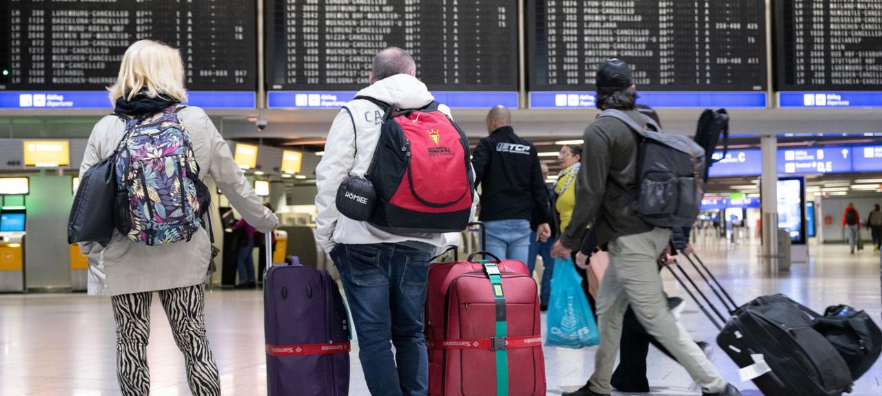 Passagiere stehen mit ihren Koffern vor der Anzeigetafel im Terminal 1 des Flughafens. (Archivbild vom 20. Februar 2024)
