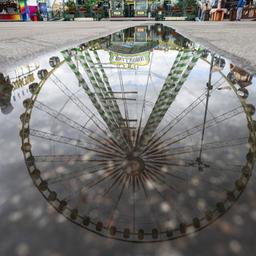 Ein Riesenrad auf dem Cannstatter Wasen in Stuttgart spiegelt sich in einer Pfütze.