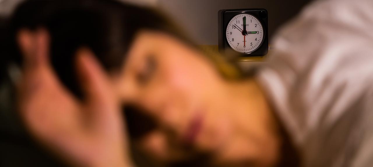 Eine Frau schläft, im Hintergrund steht ein Wecker