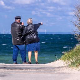 Ein Rentnerpaar steht am ansonsten menschenleeren Strand und schaut aufs Meer.