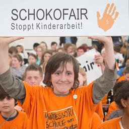 Ein Junge ein Plakat mit der Aufschrift "SCHOKOFAIR Stoppt Kinderarbeit!" in die Höhe.