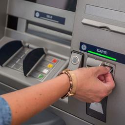 Eine Frau hebt Bargeld mit einer EC Karte an einem Bankautomaten ab.