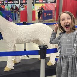 Ein fröhliches Mädchen steht vor einem Einhorn aus Lego