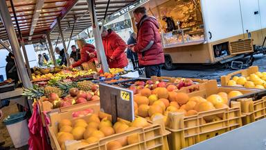 Kunden kaufen an einem Gemüsestand auf einem Wochenmarkt ein.